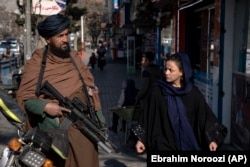 A woman walks past a Taliban fighter in Kabul.