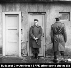 A detained man stands inside a chalk outline at the recreation of a crime scene in Budapest.