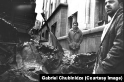 Men look over a destroyed vehicle.