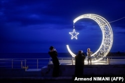 A family takes photos next to a crescent moon-shaped decoration placed in the town of Ulcinj on April 9, during the Muslim fasting month of Ramadan.