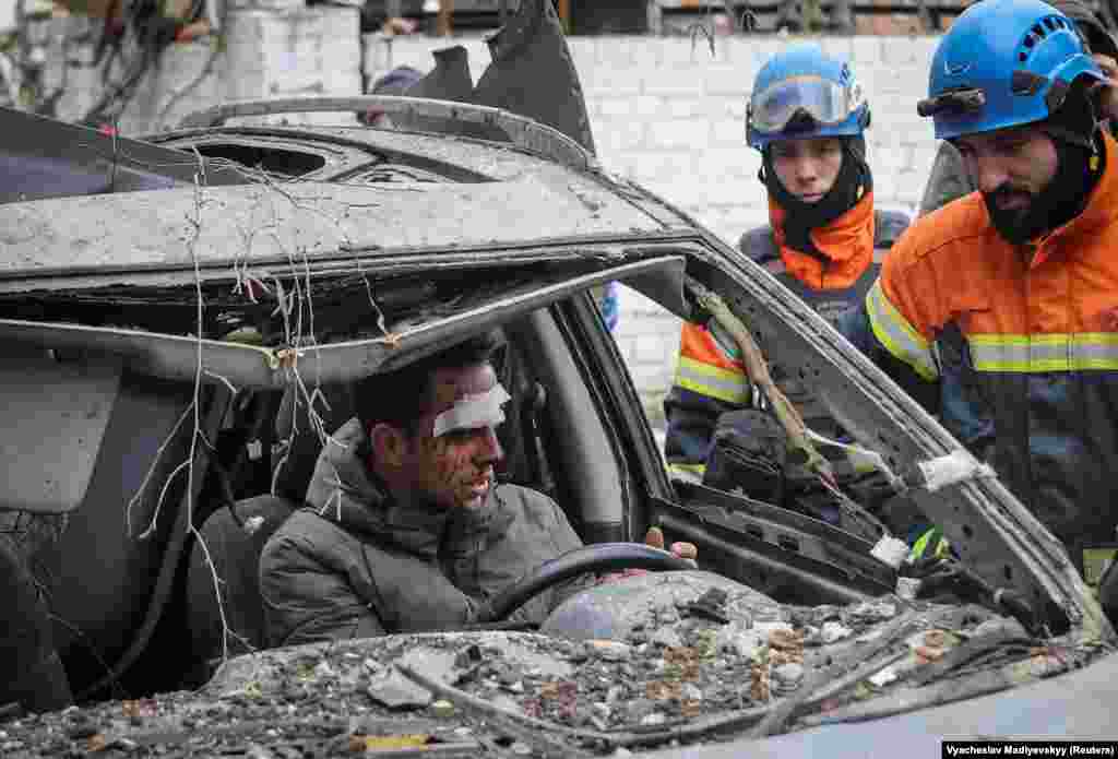 A wounded Kharkiv resident examines his destroyed car outside a residential building...