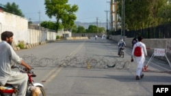 Residents appear on a street partially blocked by barbed wire a day after a Pakistani Army garrison was attacked by a suicide bombing squad in Bannu. 