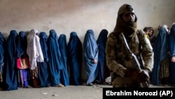 A Taliban fighter stands guard as women wait to receive food rations distributed by a humanitarian aid group in Kabul last month.