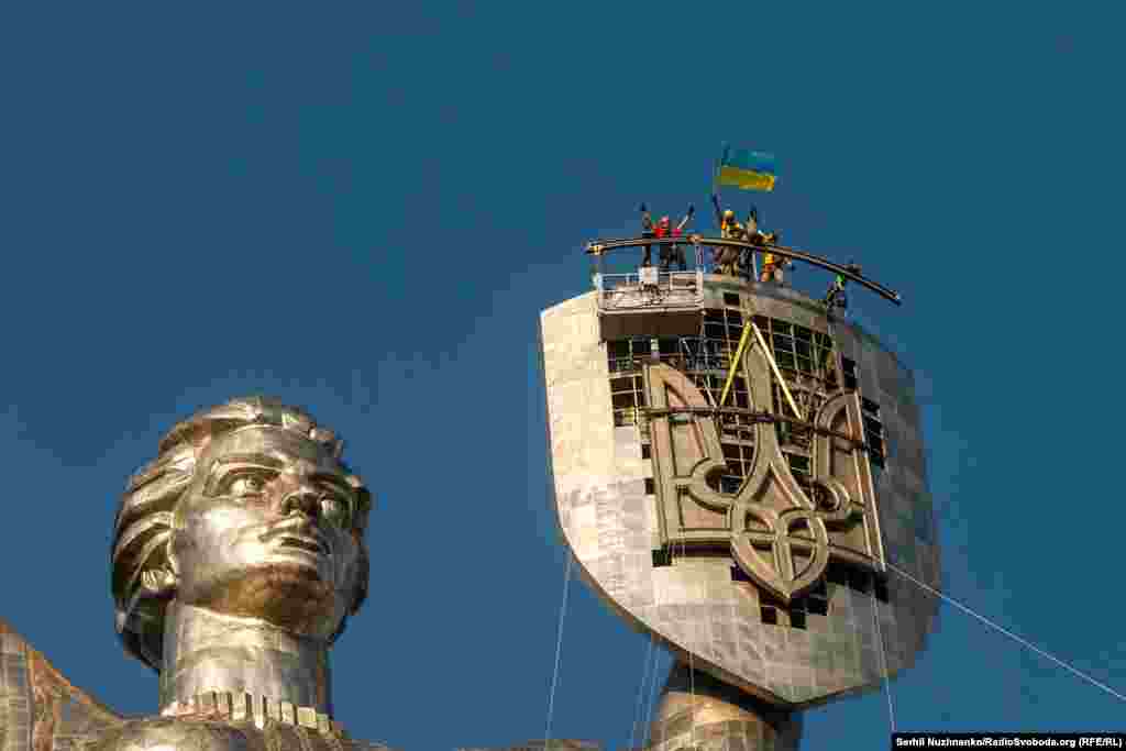 Workers celebrate after the installation of the Ukrainian trident on the shield of Kyiv&#39;s motherland monument on August 6, 2023. The massive trident replaced a Soviet emblem.&nbsp;