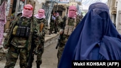 Taliban security personnel stand guard as a burqa-clad Afghan woman walks along a street in the Baharak district of northeastern Badakhshan Province in February.