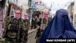 Taliban security personnel patrol a street as a burqa-clad Afghan woman walks by in Badakhshan Province (file photo).