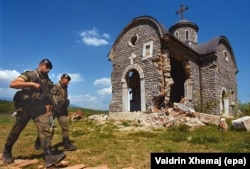 Spanish peacekeepers walk past a damaged church in Osojan in May 2000.