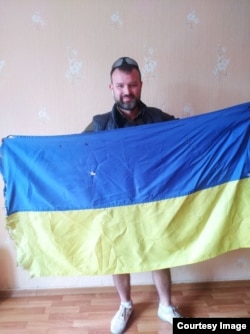 French teacher and student media center director Ivan Shybkov with the Ukrainian flag he recovered from the damaged Harant school building in Lysychansk