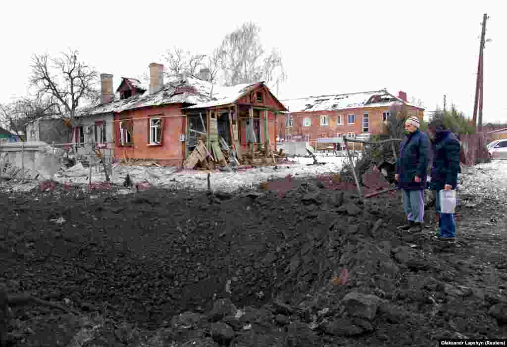 People stand next to a shell crater in front of a house damaged by recent shelling in Kharkiv on March 6.