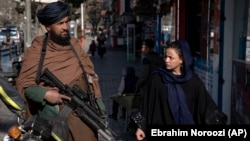 A Taliban fighter security officer stands on duty as a woman walks past him in Kabul. (file photo)