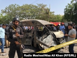 A policeman guards a burnt van after a suicide bombing attack inside Karachi University on April 26.