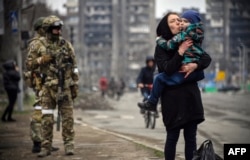 A woman carrying a child walks past Russian soldiers in the street in Mariupol on April 12.