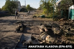 Local residents pass by the dead bodies of Russian soldiers on a street in Lyman on October 6, shortly after the town was liberated.