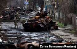 A soldier takes a photograph of his comrade as he poses beside a destroyed Russian tank and armored vehicles in Bucha on April 2.