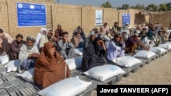 People sit beside sacks of food grains distributed as aid by the World Food Program in Kandahar on October 19.