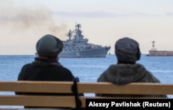 Two women sit on a bench as the Russian Navy's guided missile cruiser Moskva sails back into harbor in Sevastopol, Crimea, after tracking NATO warships in the Black Sea on November 16, 2021.