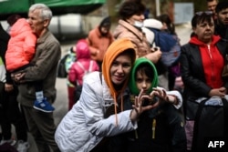 A Ukrainian refugee makes a love sign as she waits to board a bus along with her son bound for Germany in the Moldovan capital, Chisinau, on April 13, 2022.