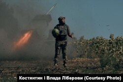 A Ukrainian soldier holds a watermelon while a multiple rocket launcher fires in the background.