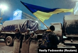 A demonstrator holds a Ukrainian flag as he stands next to Interior Ministry personnel on December 9. Skirmishes with riot police failed to dislodge thousands of protesters, despite the harsh winter weather.