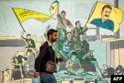 A man walks past a mural depicting supporters of the Kurdish-led SDF in the northeastern city of Qamishli on December 16.