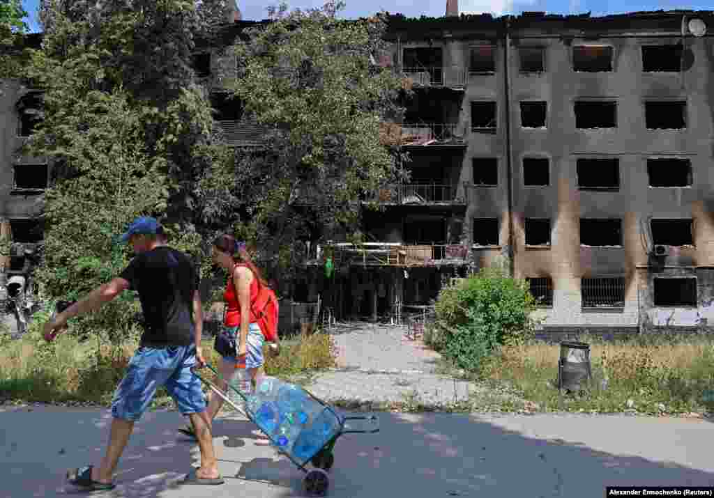 Local residents carry bottles of water past destroyed residential buildings.