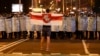 A protester holds a forbidden red-and-white Belarusian flag as he stands in front of a police line during a rally after the disputed Belarusian presidential election in Minsk in August 2020.