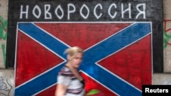 A woman walks past graffiti depicting a Novorossiya (New Russia) flag.