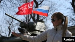 A woman feeds a pigeon near a monument displaying a Soviet-era tank as well as a Russian flag in the Crimean capital Simferopol on March 15.