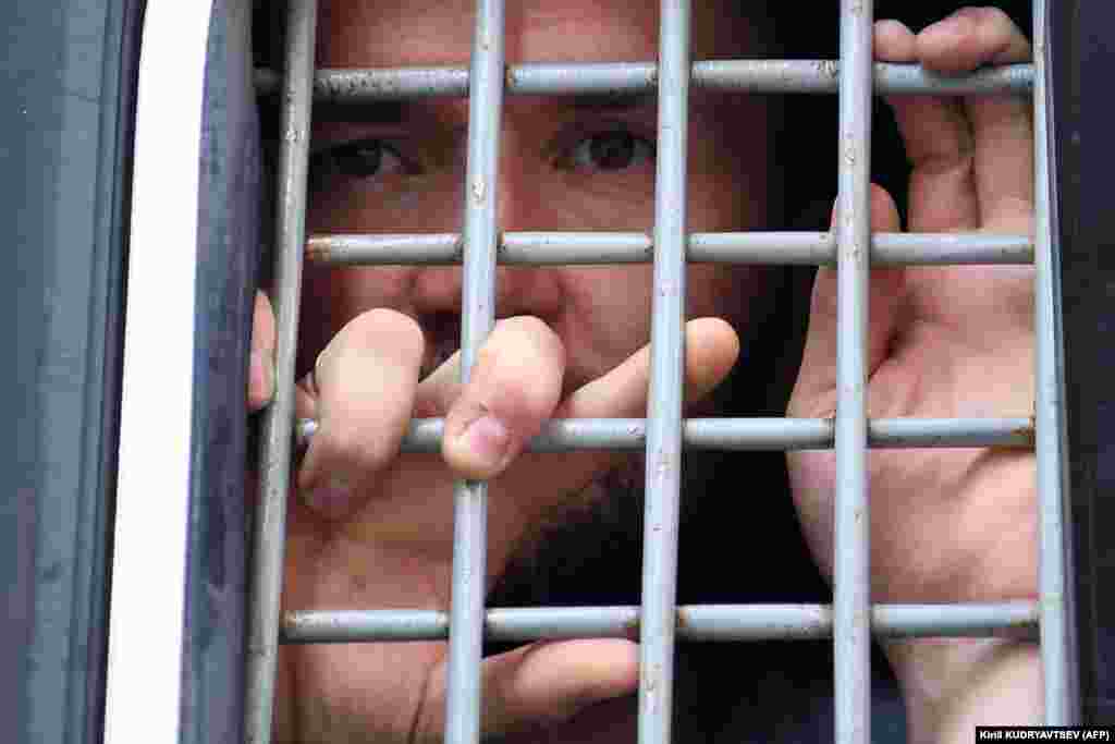 A detained protester looks out from the barred window of a police van.&nbsp;