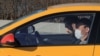 A driver from the Yandex.taxi ride-sharing service sits inside his car in Moscow on March 26. One driver said he and his colleagues have been encouraged to disinfect the interiors of their vehicles but that there have been no instructions on how often the cars should be disinfected, and no one is checking to see that it is done at all.