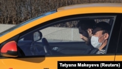 A driver from the Yandex.taxi ride-sharing service sits inside his car in Moscow on March 26. One driver said he and his colleagues have been encouraged to disinfect the interiors of their vehicles but that there have been no instructions on how often the cars should be disinfected, and no one is checking to see that it is done at all.