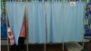 A little girl peeks around the curtain as a family member casts her ballot. 