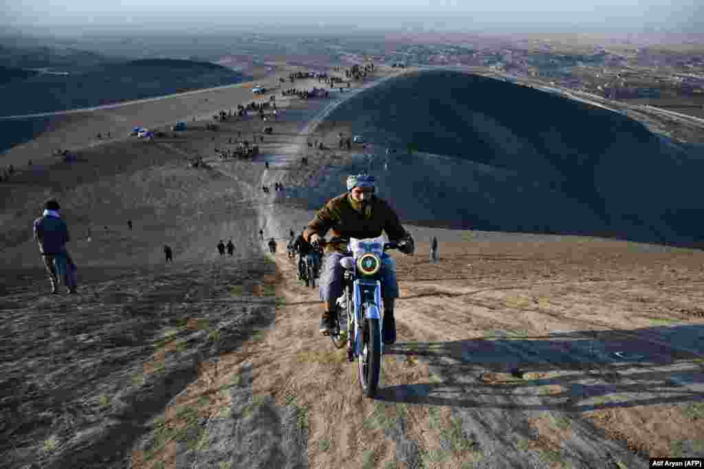 Afghan men show their skills as they ride motorcycles along a hillside on the outskirts of Mazar-i-Sharif.&nbsp;