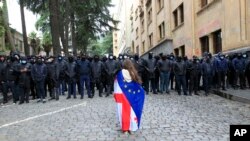 A demonstrator draped in the Georgian national and EU flags stands in front of police blocking the way to the parliament building in Tbilisi during an opposition protest against a controversial "foreign agent" law in May. 