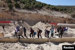 People carry their belongings while walking next to the rubble, after an Israeli strike, at the Masnaa border crossing.