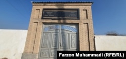 A tall gate leading to the Jewish cemetery in Khujand features a sign in Tajik, Hebrew, and English.