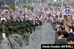 Security forces standing behind barbed wire observe protesters during another mass rally in Minsk on August 23.