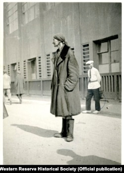 A photo of an emaciated woman outside a factory in Ukraine taken by Whiting Williams in August 1933. The fact that she is dressed in a heavy overcoat and boots at the height of summer suggests that she may have been homeless and forced to wear and carry all her belongings with her. A caption by Whiting on the back of the original photo describes the woman as "one of the weaker ones whose very life depends on, not the present crop but the present harvest."