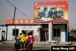 A Uyghur woman in Xinjiang uses an electric-powered scooter to fetch school children as they ride past a picture showing Chinese leader Xi Jinping joining hands with a group of Uyghur elders.