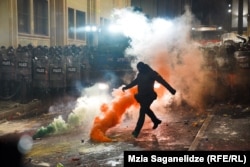 A masked policeman kicks a smoke bomb alongside Georgia's parliament building in Tbilisi on November 29 during the second night of protests that erupted after the Georgian government announced the suspension of EU accession talks.