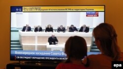 A woman and her daughter watch television during a discussion on the proposal of Russian President Vladimir Putin and the use of Russian armed forces in Ukraine in parliament in Moscow on March 1.