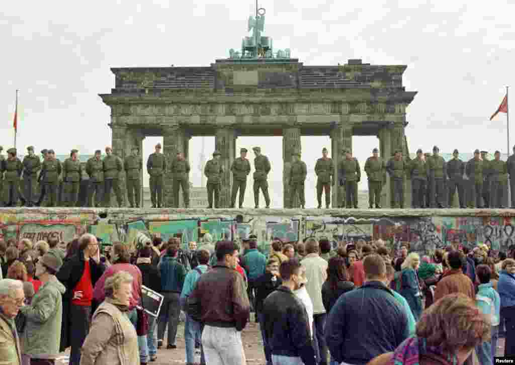 East Berlin border guards stand atop the Berlin Wall in front of the Brandenburg Gate on November 11, 1989. Two days earlier, on November 9, the wall was breached by thousands of Germans after an East German official indicated that travel restrictions between East and West Germany were to be ended &quot;without delay.&quot;&nbsp;&nbsp;