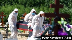 Gravediggers wearing personal protective equipment bury a person who died from COVID-19, in a cemetery on the outskirts of St. Petersburg. 