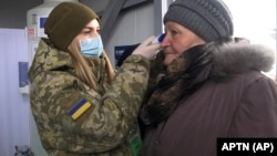 A Ukrainian soldier checks the temperature of an elderly woman at a checkpoint in Mayorsk in the Donetsk region last month.