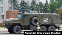 An elderly woman looks at an armored truck belonging to pro-Russian troops parked near Ukraine's former regional council building in the Russia-controlled city of Kherson on July 25.