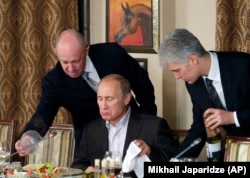 Yevgeny Prigozhin (left) assists then-Russian Prime Minister Vladimir Putin during a dinner with foreign scholars and journalists at a restaurant outside Moscow in 2011.