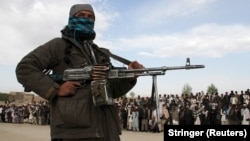 A Taliban fighter and onlookers attend the execution of three men in Ghazni Province in April 2015.