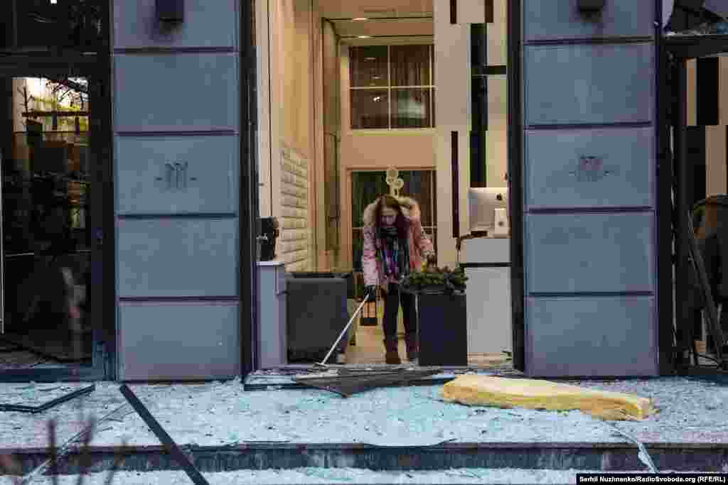 A shop worker clears glass shattered across the sidewalk.