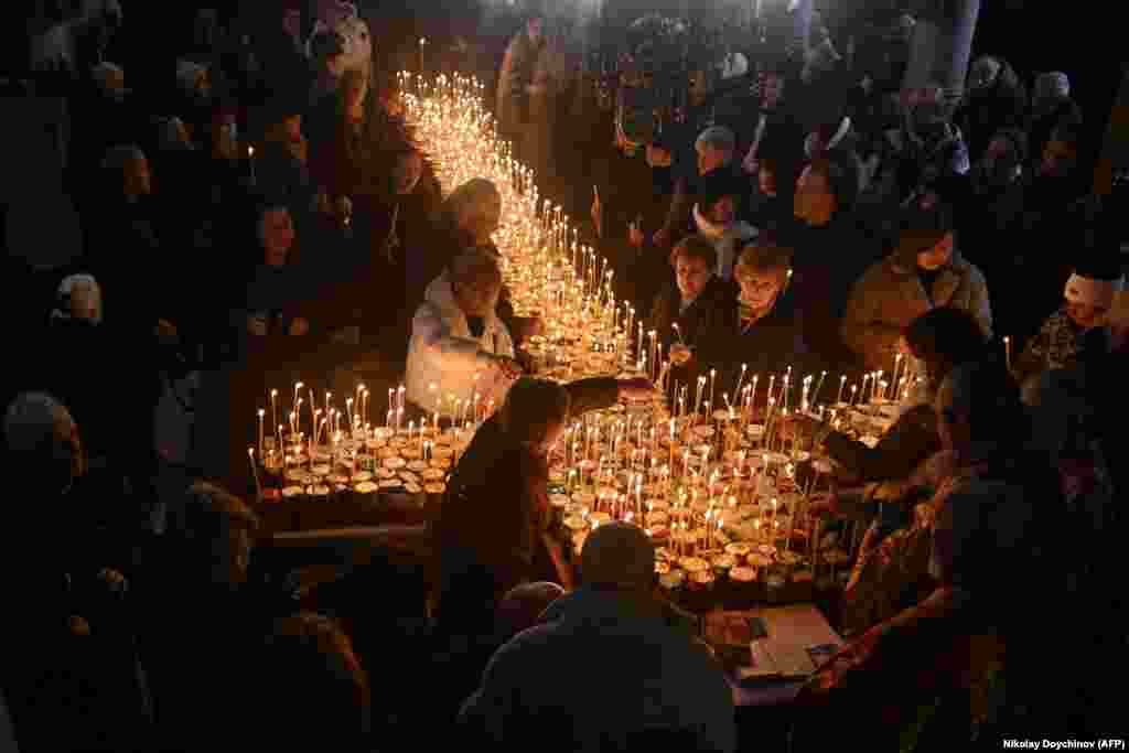 Believers light candles on a cross-shaped platform covered with candles attached to jars of honey during a ceremony marking the day of St. Haralampi, Orthodox patron saint of beekeepers, at the Church of the Blessed Virgin in Blagoevgrad, eastern Bulgaria.