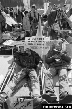 A student hunger striker wearing symbolic shackles. The sign reads: “We won’t eat, we won’t drink until we will live freely."